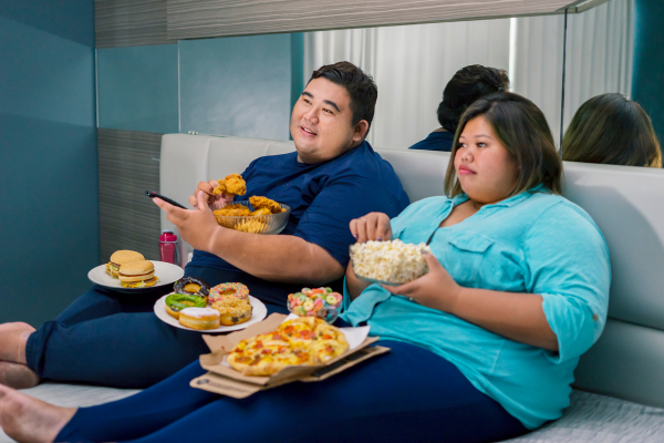 Plus Size Couple Eating Junk Food While Watching TV, discussing symptoms of infertility