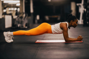 Fit African American woman performing a plank in a gym, illustrating the physical effort and intensity discussed in the context of the Impact of Intense Exercise on Fertility